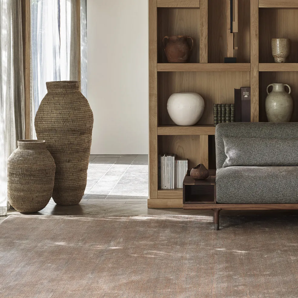 Wohnraum mit Holzregal, geflochtenen Vasen, grauem Sofa und Teppich