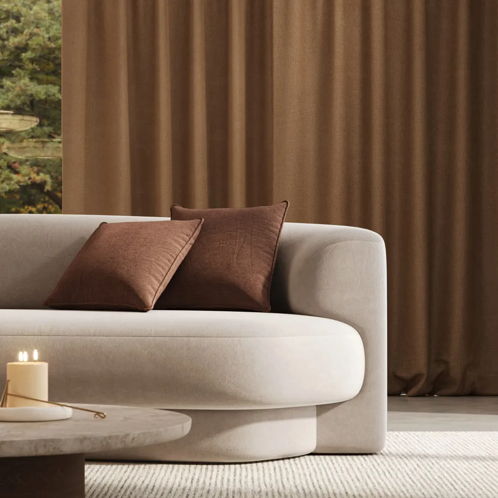 Helles Sofa mit rostbraunen Kissen vor einem bodenlangen Vorhang